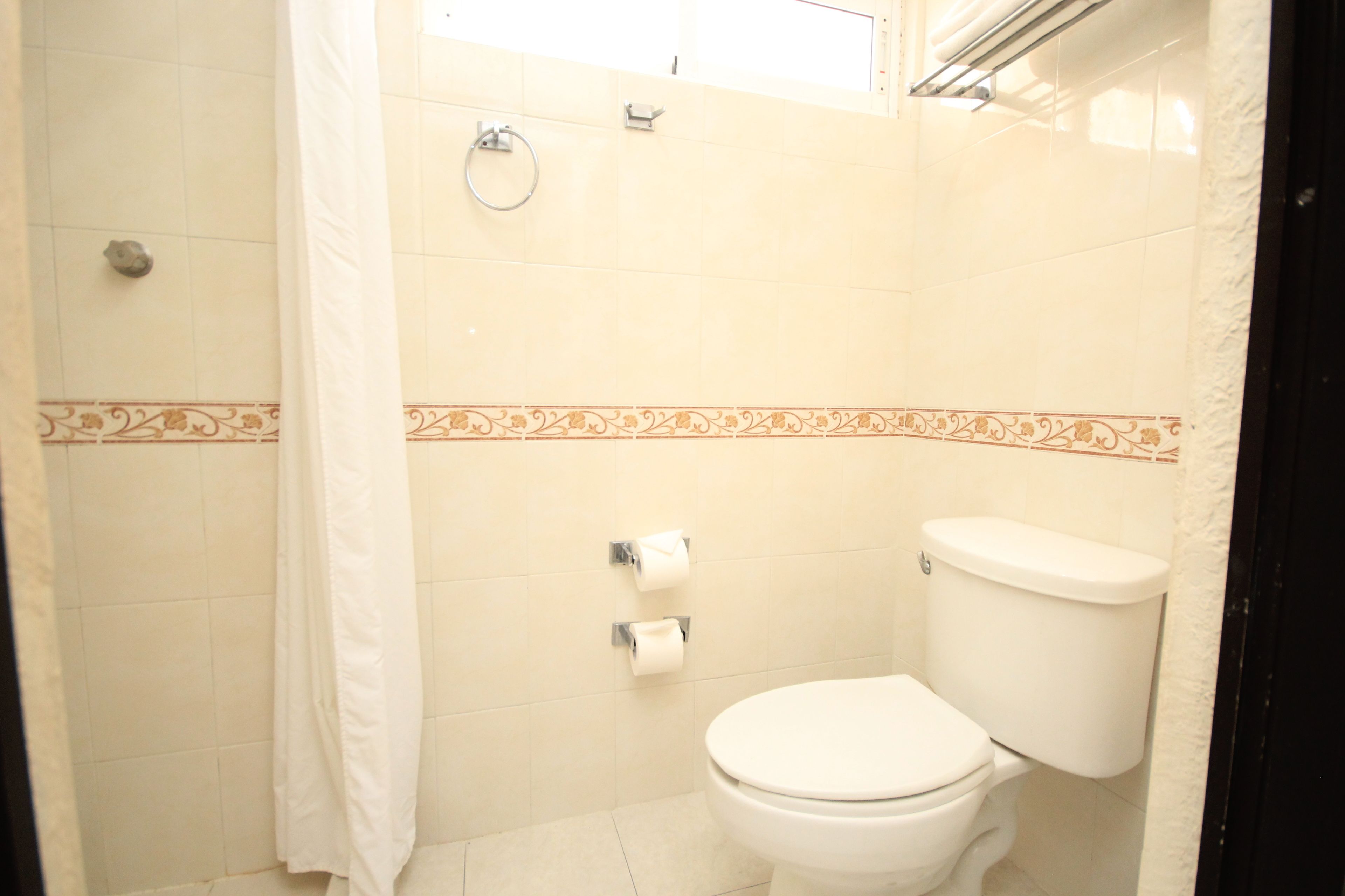 A bathroom with a toilet, two rolls of toilet paper, a towel rack, and a shower curtain.