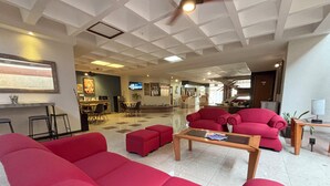 Un vestíbulo de hotel con un sofá rojo grande, una mesa de centro y una pantalla de televisión.