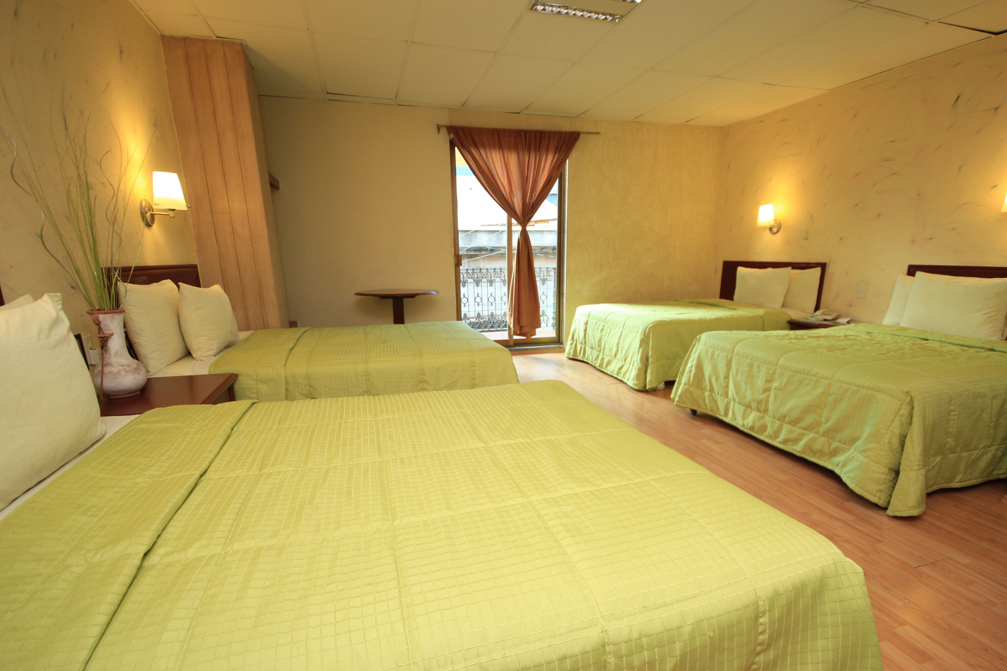 A hotel room with two beds, a small table, a potted plant, and a window with curtains.