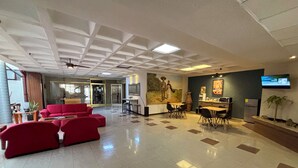 Un vestíbulo amplio con un conjunto de sofás rojos, un área de comedor, un mural y un televisor en la pared.