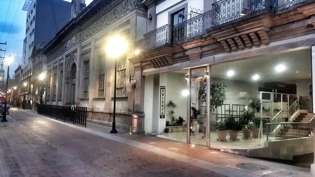 Un hotel con entrada de cristal, una escalera que conduce a la entrada y un balcón con barandilla de hierro forjado.