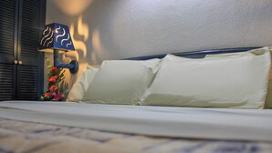Un lit avec des oreillers blancs et une lampe bleue, agrémenté d’un arrangement floral placé à côté.