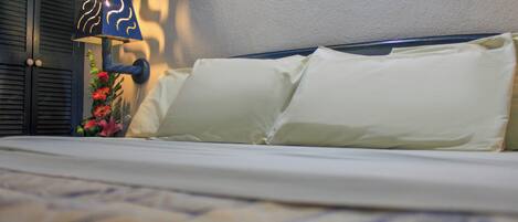 A bed with white pillows and a blue lamp with a floral arrangement beside it.