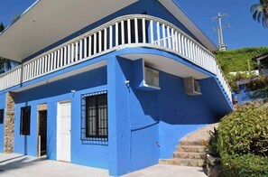 Un bâtiment bleu avec un balcon blanc, une porte et une fenêtre avec des barreaux.