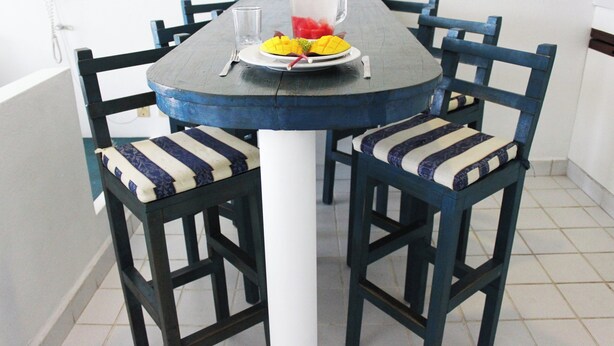 Une table à manger avec des chaises, une carafe et une assiette de fruits.