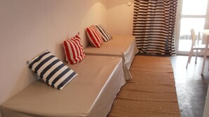A room with two single beds, a small table, a chair, a lamp, and a window with curtains. - Departamentos El Terrado II (Las Grutas)