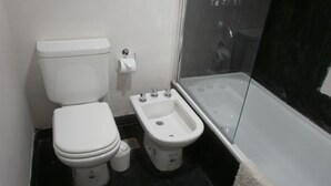 A bathroom with a toilet, bidet, and a glass-enclosed shower area. - Departamentos El Terrado II (Las Grutas)