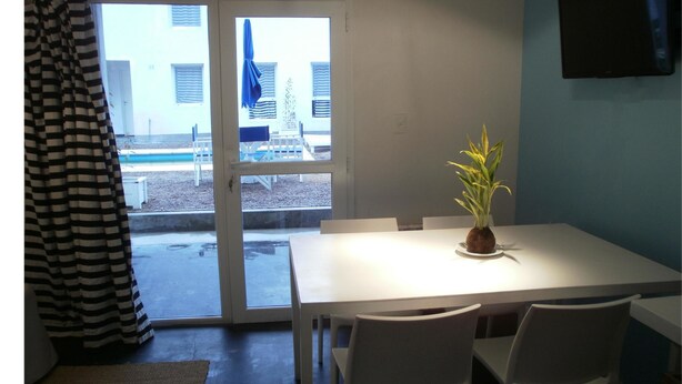 A dining area with a white table and chairs, a potted plant, and a view through a glass door to an outdoor seating area. - Departamentos El Terrado II (Las Grutas)