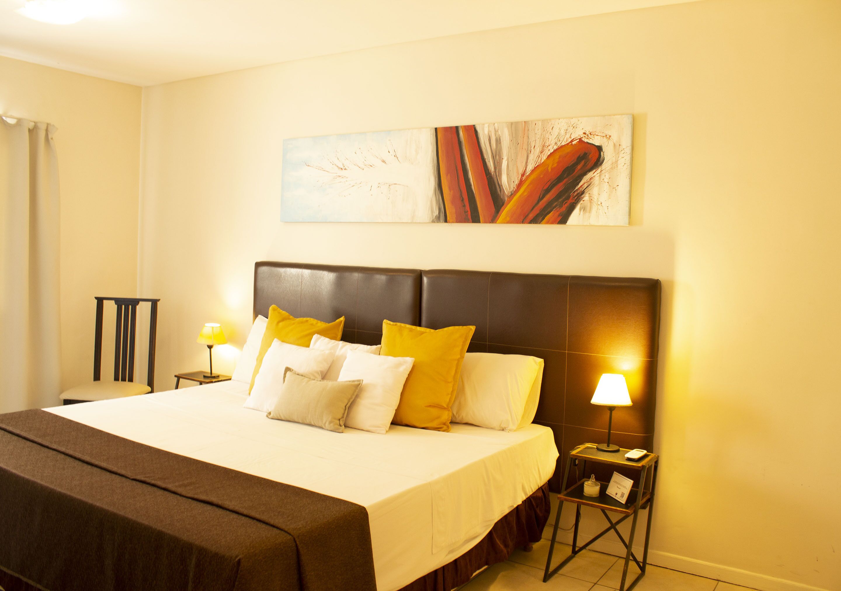 A hotel room with a large bed, two bedside tables with lamps, a headboard, and a painting on the wall.