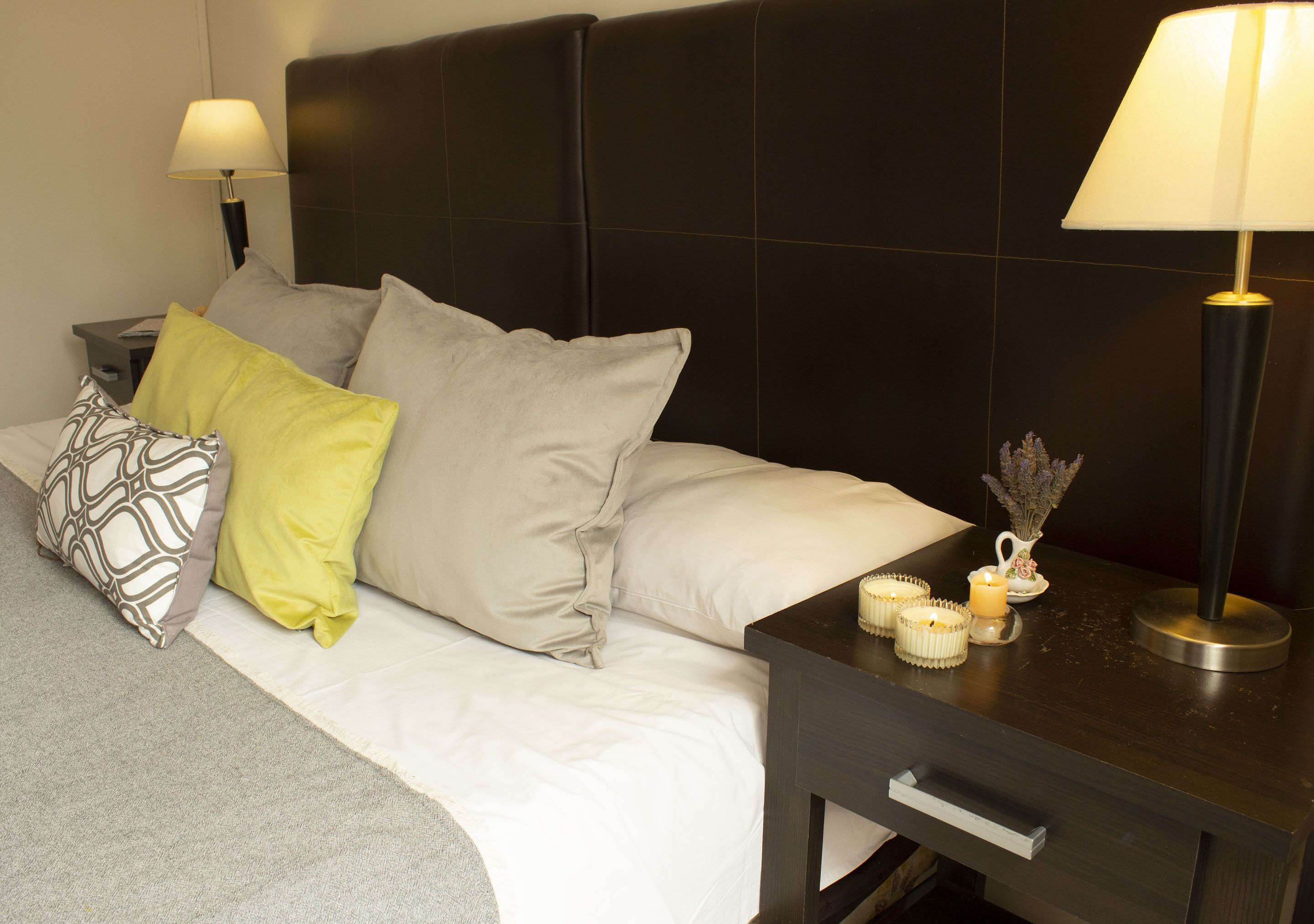 A neatly made bed with pillows, a bedside table with a lamp, and a small vase with flowers.