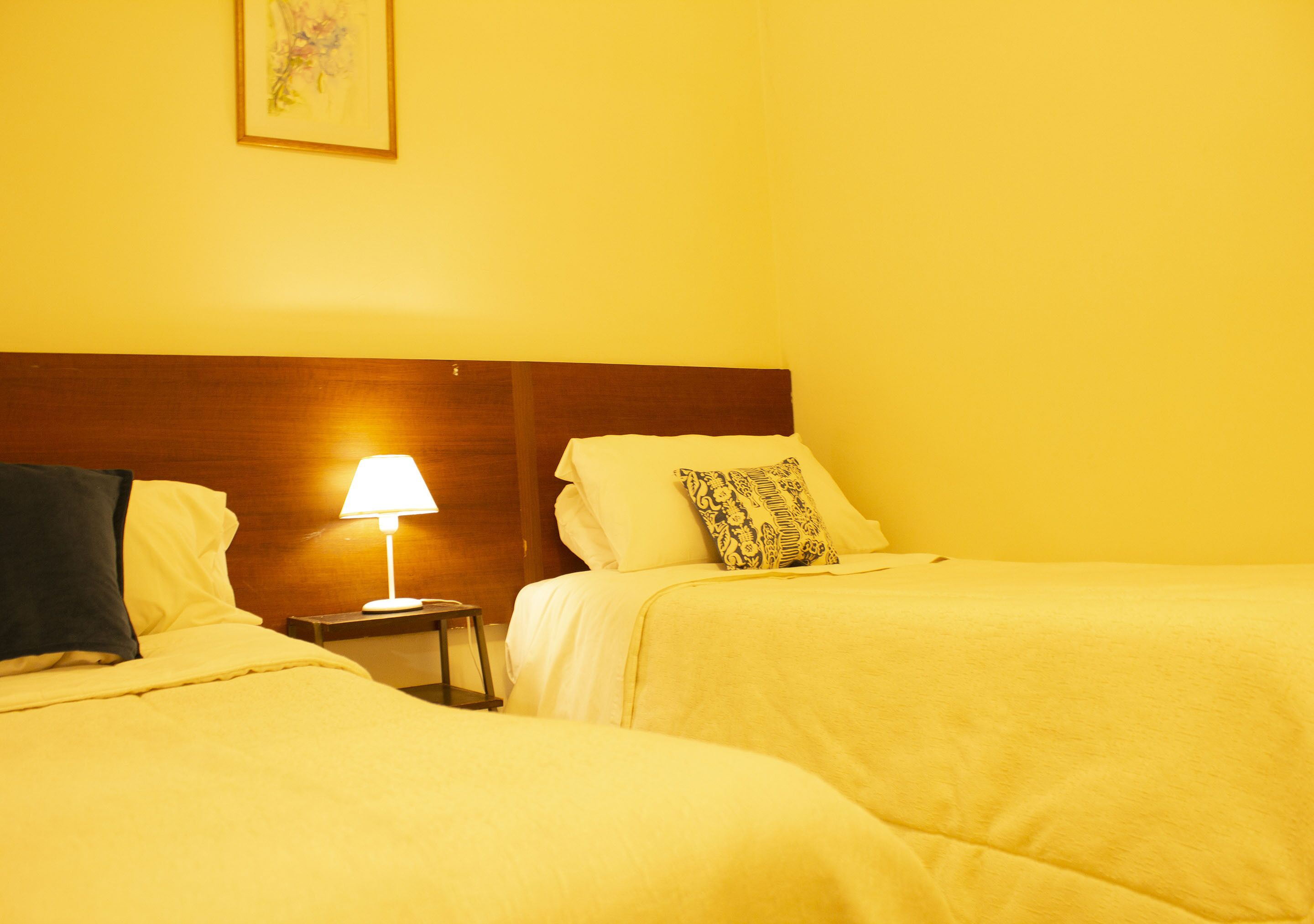 Een hotelkamer met twee bedden, een nachtkastje met een lamp en een lijst aan de muur.
