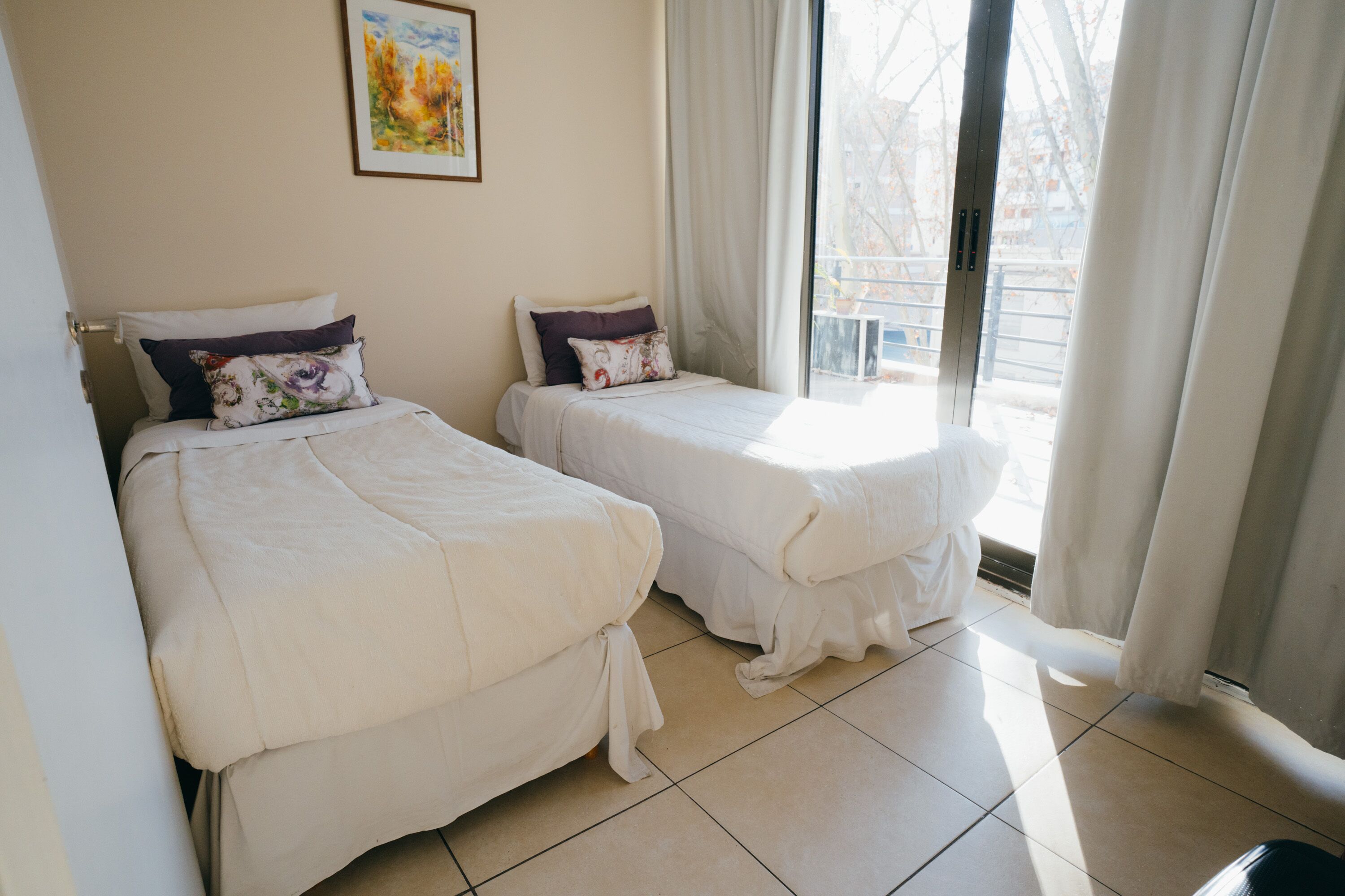 Una habitación de hotel con dos camas, una ventana con cortinas y un cuadro en la pared.