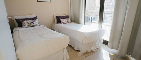 A hotel room with two beds, a window with curtains, and a painting on the wall.