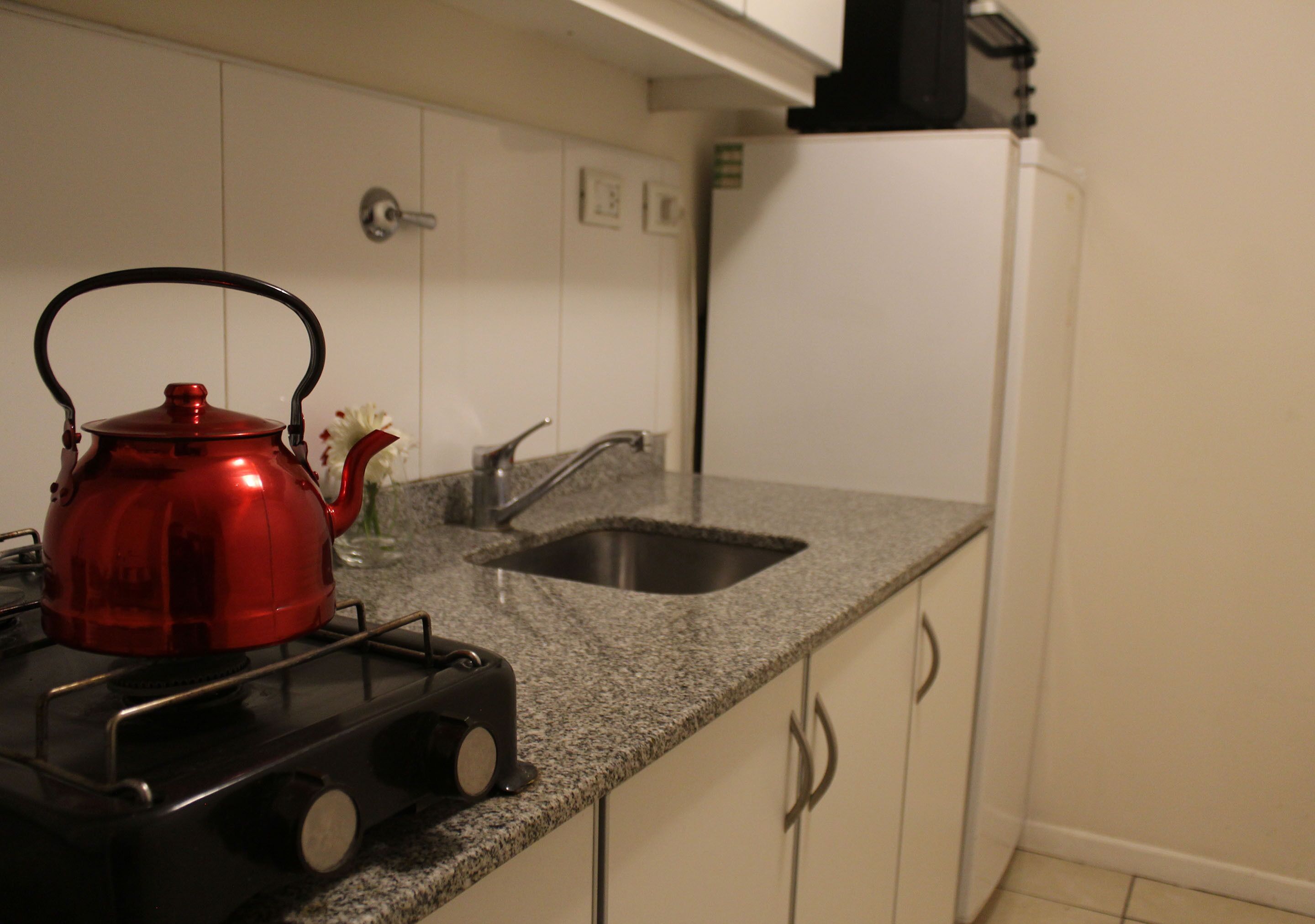 Une cuisine avec une bouilloire rouge sur la cuisinière, un évier et des armoires blanches.