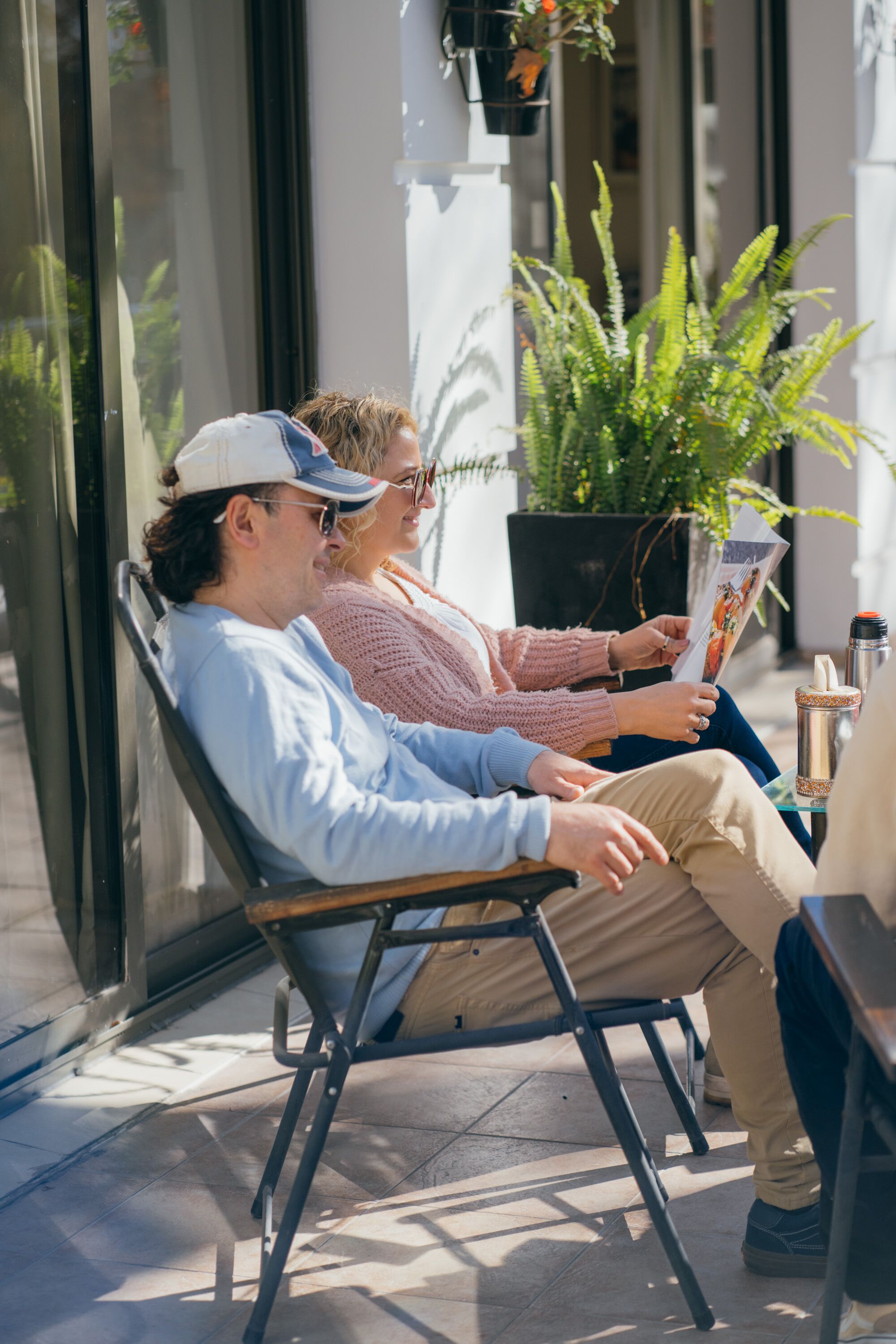 Two people sitting on a bench outside a building, reading a magazine.