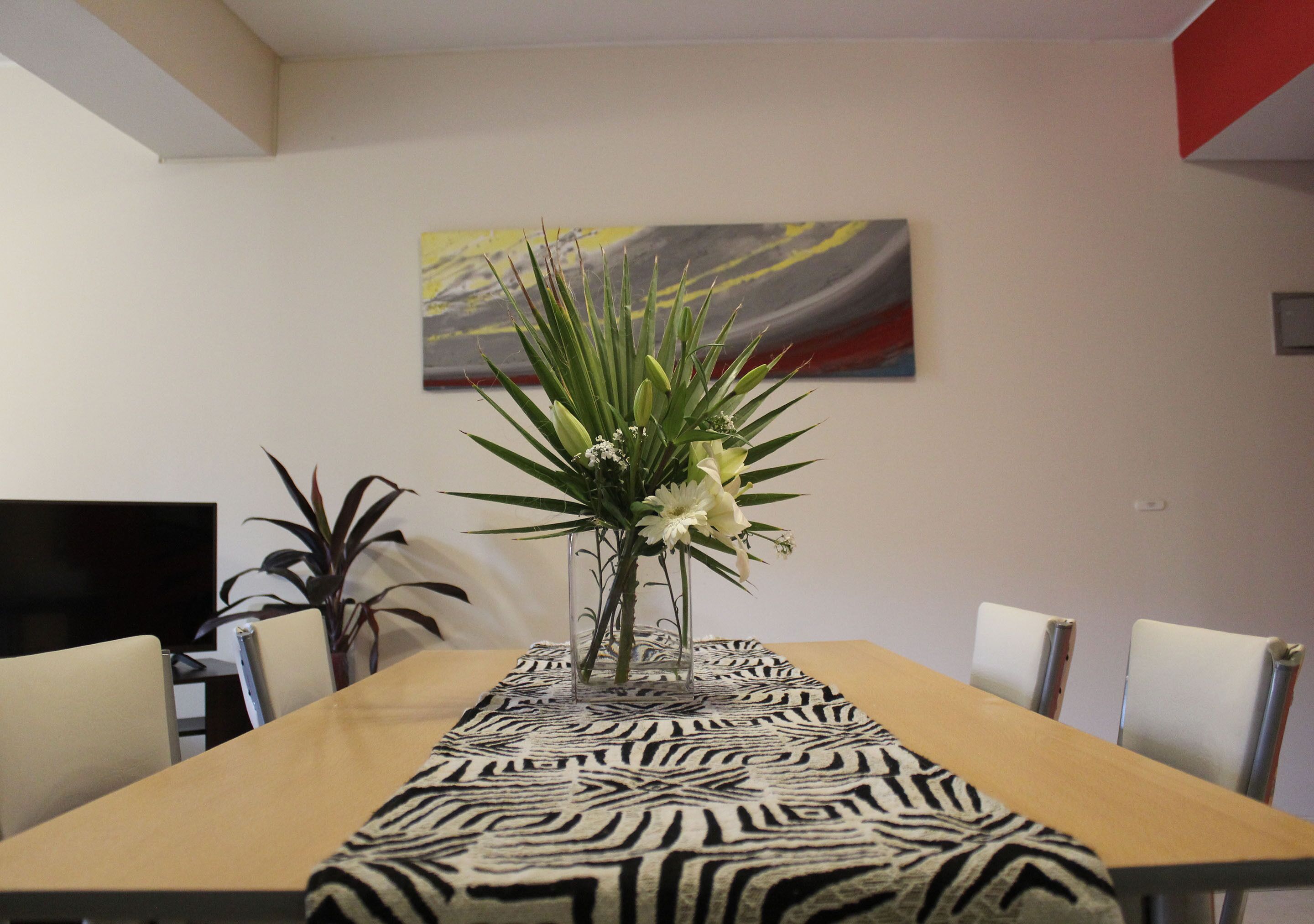 Ein Essbereich mit einer Tischläufer mit ZEBRA-Muster, einer Vase mit Blumen und einem Bild an der Wand.