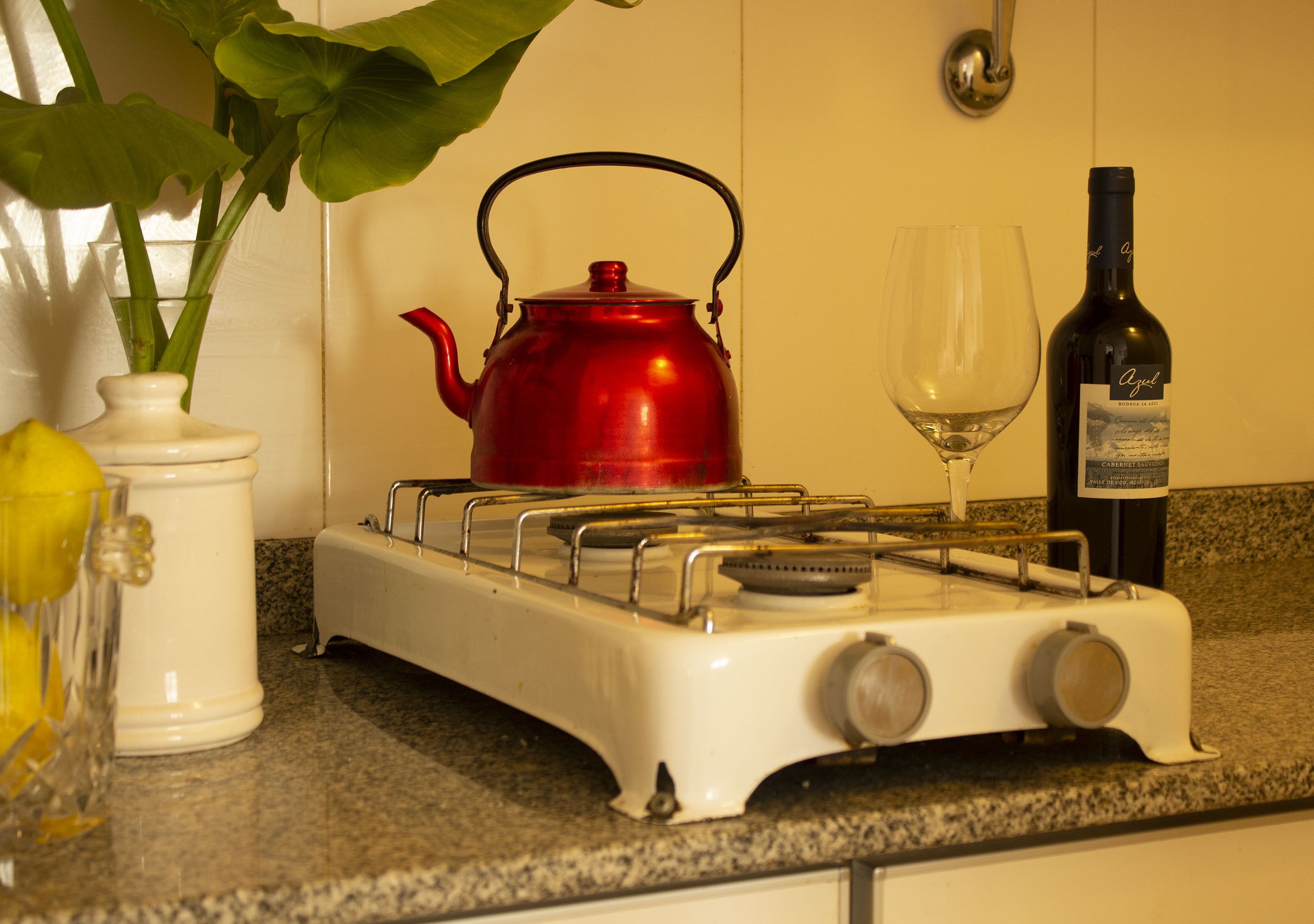A kitchen with a red kettle, a wine bottle, and a glass.