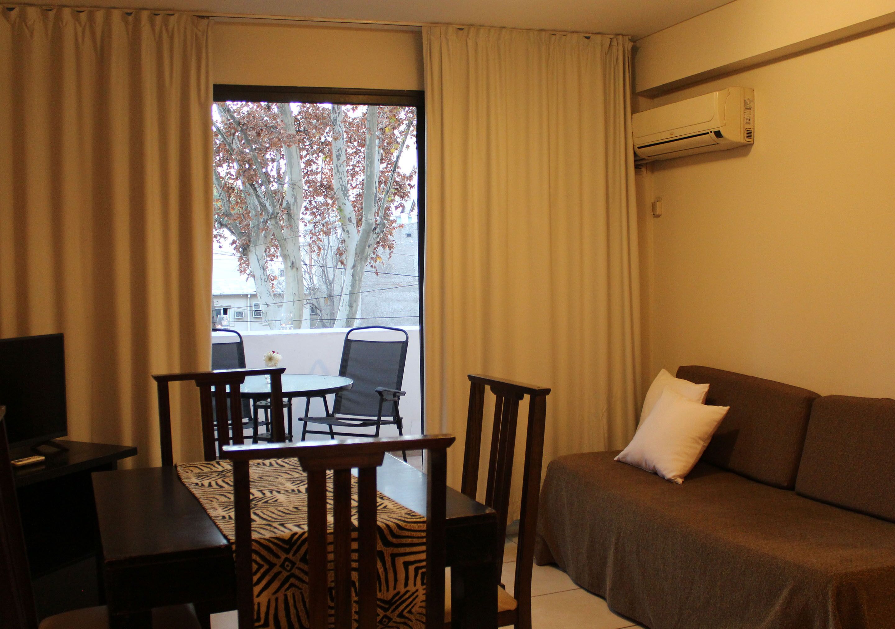 A hotel room with a sofa, a small table with chairs, a TV, and a window with curtains.