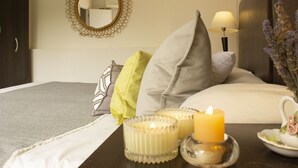 Una cama bien hecha con almohadas, una mesita de noche con una vela, una lámpara y un jarrón de flores.