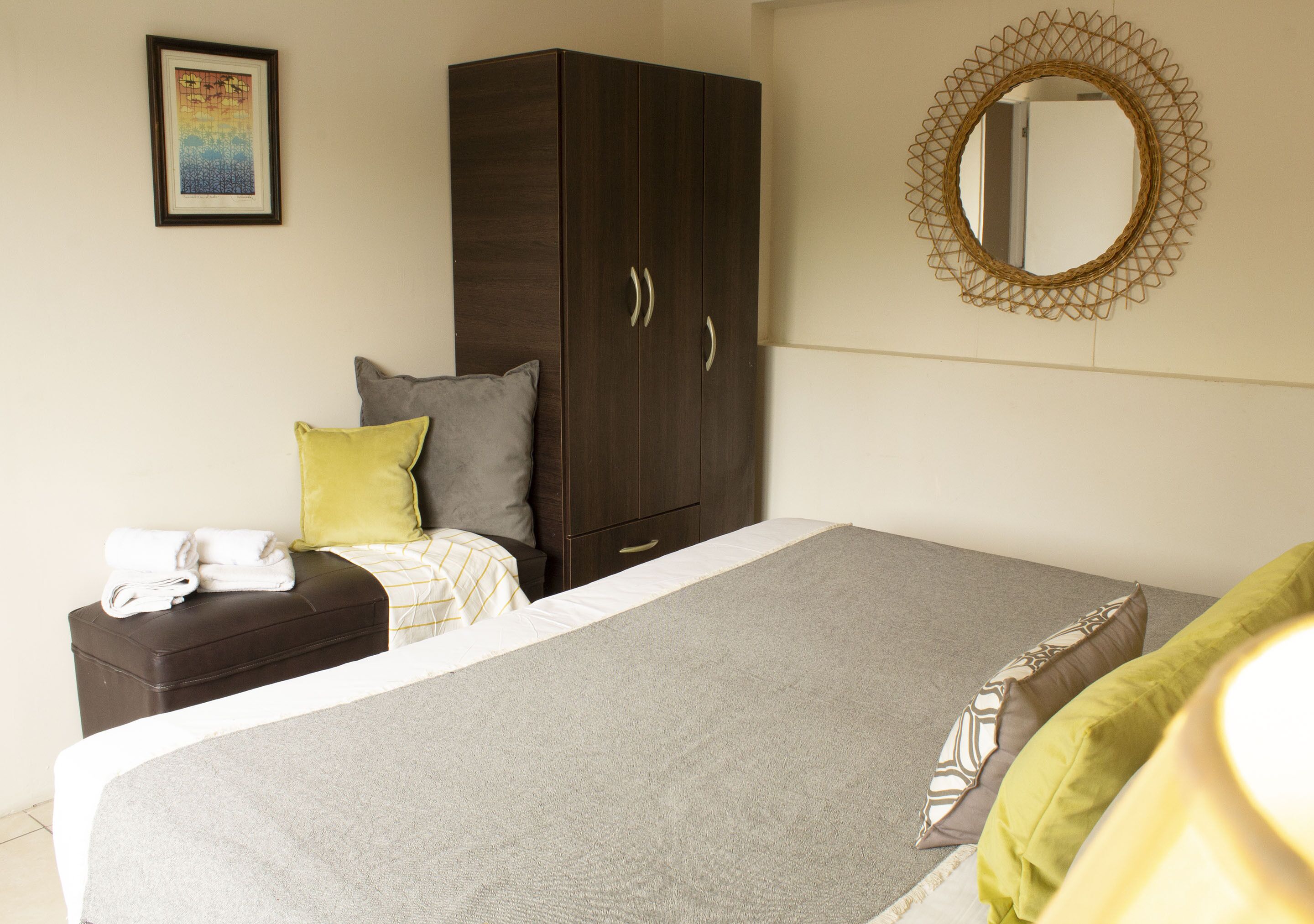 A bedroom with a bed, a wardrobe, a nightstand, a mirror, and a framed picture on the wall.