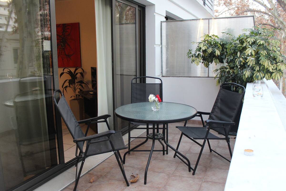 Un patio con una mesa redonda y cuatro sillas, una planta en maceta y un ventanal corredera.