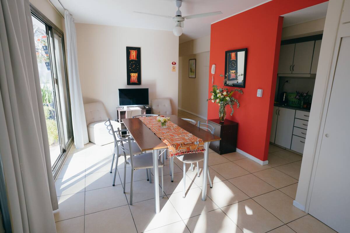 Un comedor con mesa, sillas, televisor y obras de arte en las paredes.