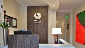 Un área de recepción con diseño moderno, que incluye un mostrador de recepción, un cartel mural para el apart hotel UVAS y un cuadro en la pared.