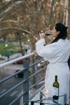 A person in a white robe sitting on a glass table outdoors, holding a wine glass. - Uvas Apart Hotel (Mendoza)