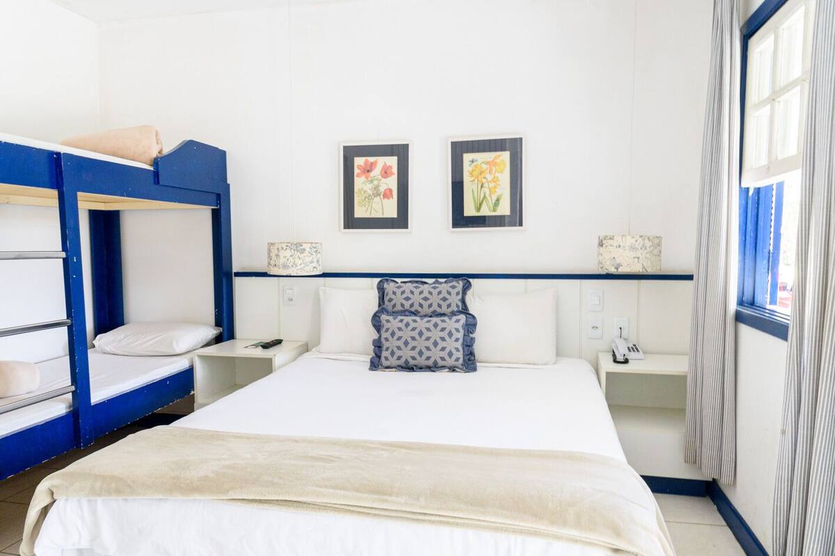 Ein Hotelzimmer mit Etagenbett, einem Einzelbett, zwei Nachttischen, einer Ablage und zwei gerahmten Bildern an der Wand.
