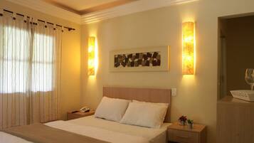 A hotel room with a bed, bedside tables, a lamp, a TV, and a window with curtains.