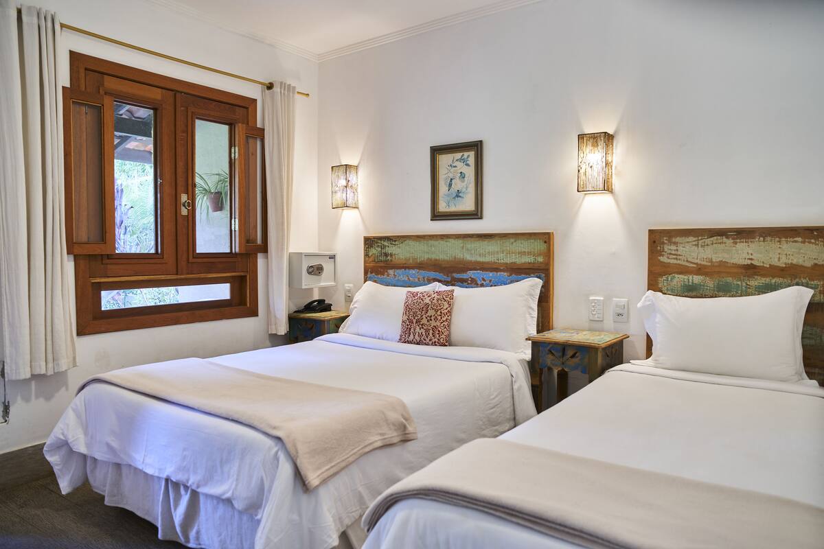 Ein Hotelzimmer mit zwei Betten, einem Holzkopfstück, einem Gemälde und einem Fenster mit Vorhängen.