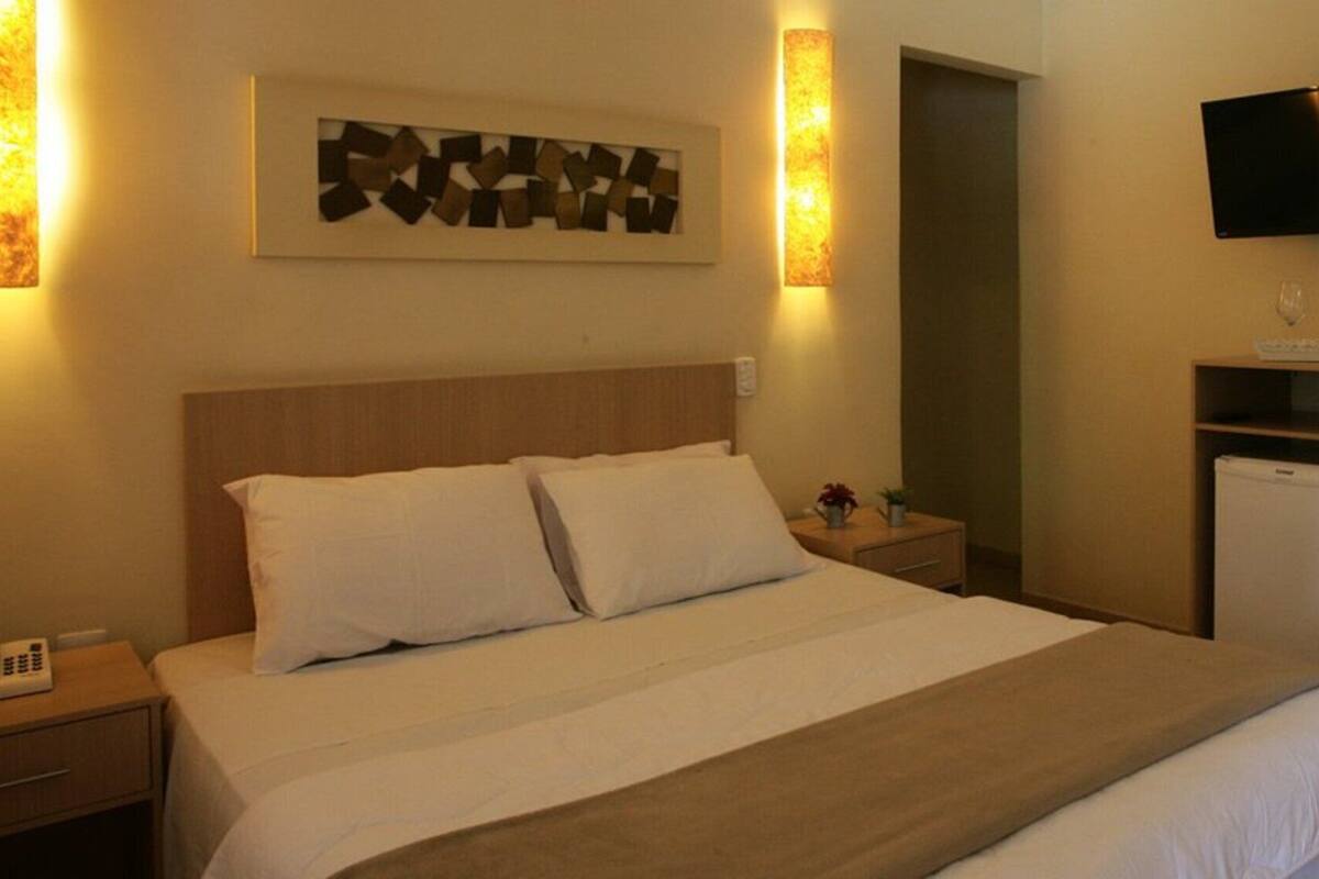 Ein Hotelzimmer mit Bett, Nachttisch, Lampe, Fernseher und Schrank.
