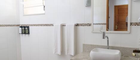 A bathroom with white tiles, a sink, a mirror, and a window with blinds.