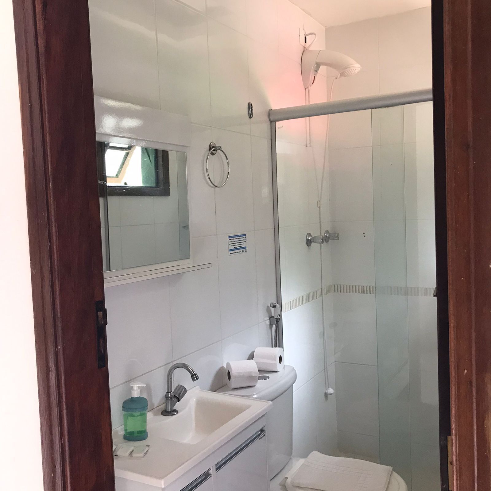 Un baño con cabina de ducha de vidrio, un lavamanos con espejo y un perchero para toallas.