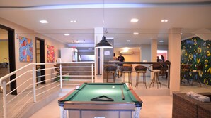 A pool table in a well-lit indoor space with a staircase, bar area, and colorful wall art. - Koze Hostel (Florianópolis)