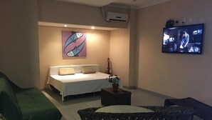 A hotel room with a bed, a green sofa, a wicker chair, a television, and a wall-mounted air conditioner. - Koze Hostel (Florianópolis)