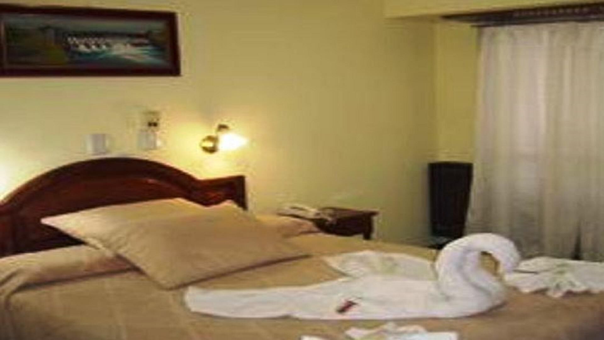 Una habitación de hotel con una cama, una mesita de noche, una lámpara y un cuadro en la pared.