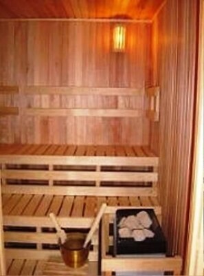 Una sauna con bancos de madera y un banco con una bandeja negra y un recipiente metálico.