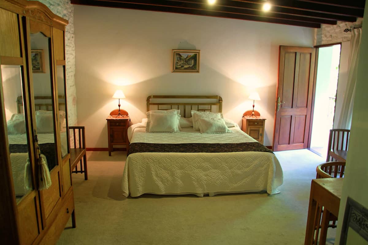 A bedroom with a large bed, two bedside tables with lamps, a wooden wardrobe, and a door leading to another room.