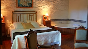 Un dormitorio con cama, mesita de noche, lámpara, silla, piso de madera, un cuadro en la pared y una bañera.
