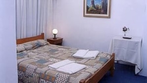 A bedroom with a bed, a nightstand, a table, and a painting on the wall. - Hotel Piedras (San Clemente)