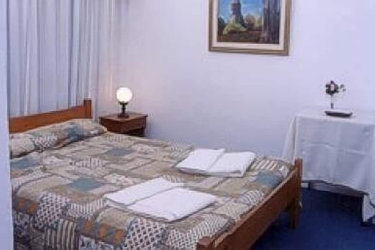 A bedroom with a bed, a nightstand, a table, and a painting on the wall.
