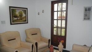 A living room with two beige armchairs, a wooden coffee table, and a beige sofa. There is a window with a view of greenery outside. - Hotel Piedras (San Clemente)