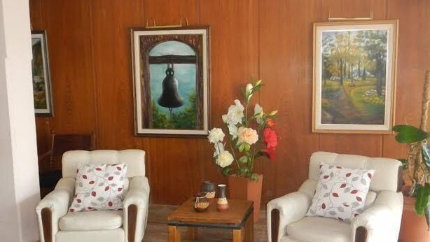 A room with two white armchairs, a wooden coffee table, and a vase of flowers. There are two framed pictures on the wall. - Hotel Piedras (San Clemente)
