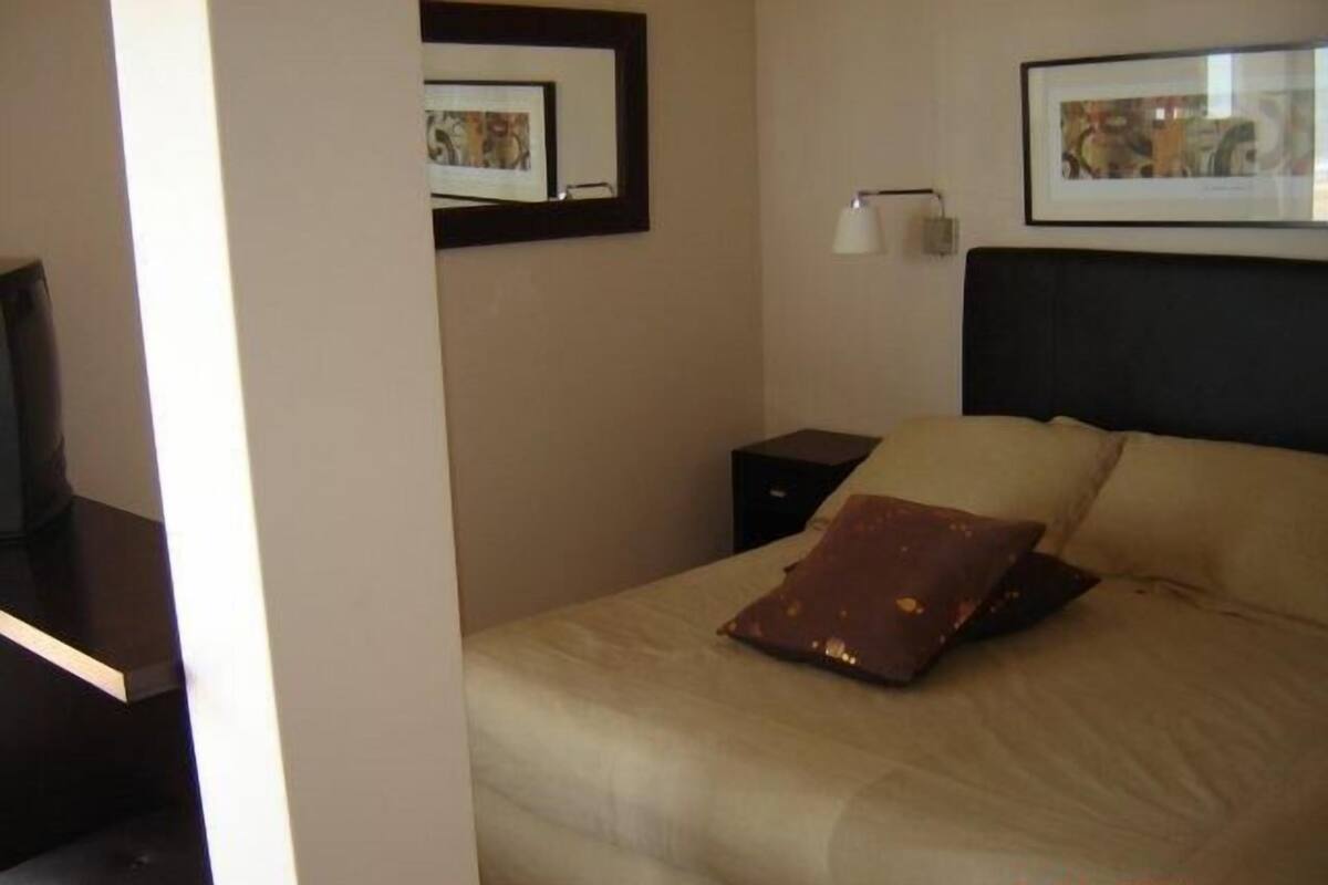 A hotel room with a bed, a nightstand, a lamp, and framed artwork on the wall.