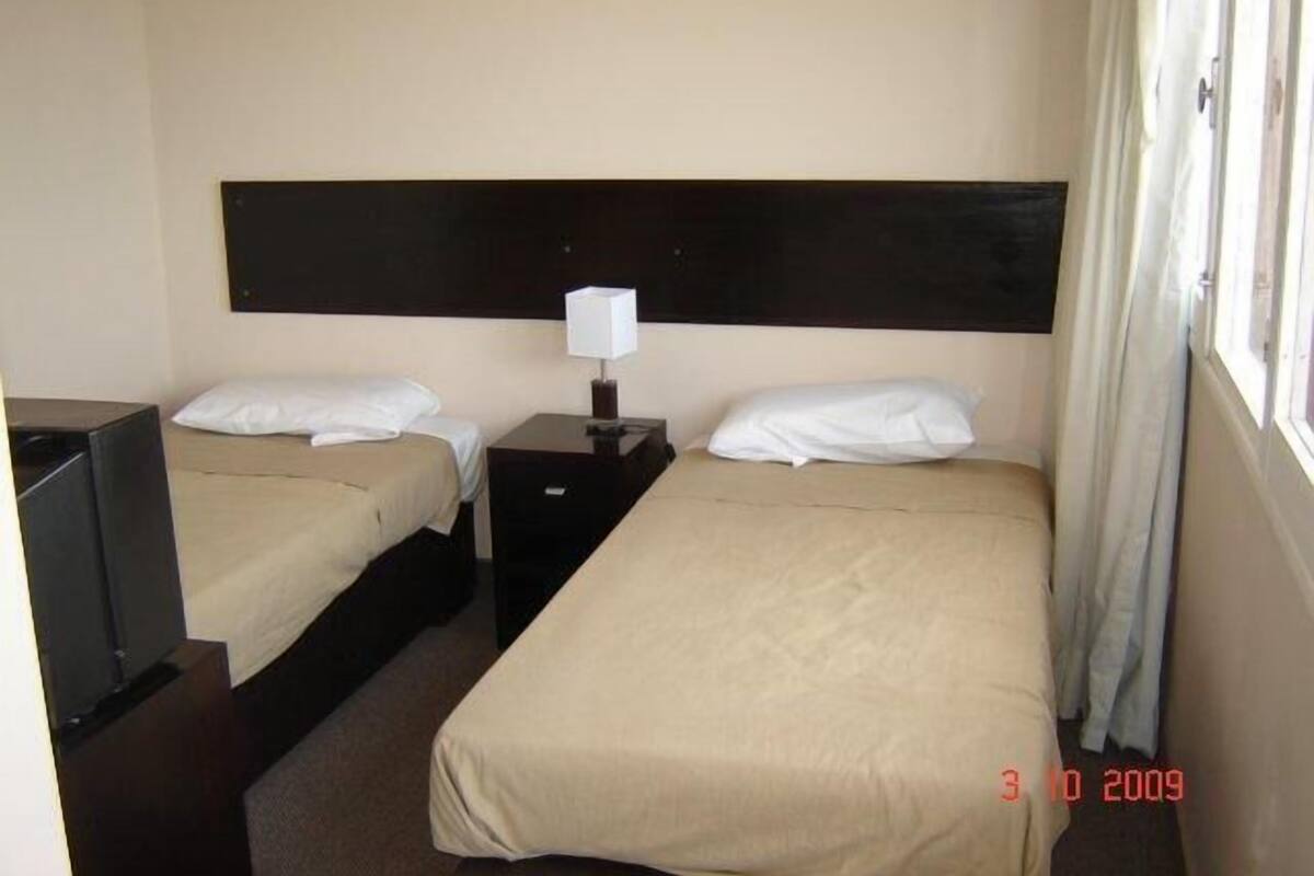A hotel room with two beds, a nightstand with a lamp, and a TV.