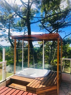 A hot tub with a wooden deck and glass enclosure, surrounded by trees and a clear sky. - Jaina Resort & Spa (Mar de Las Pampas)