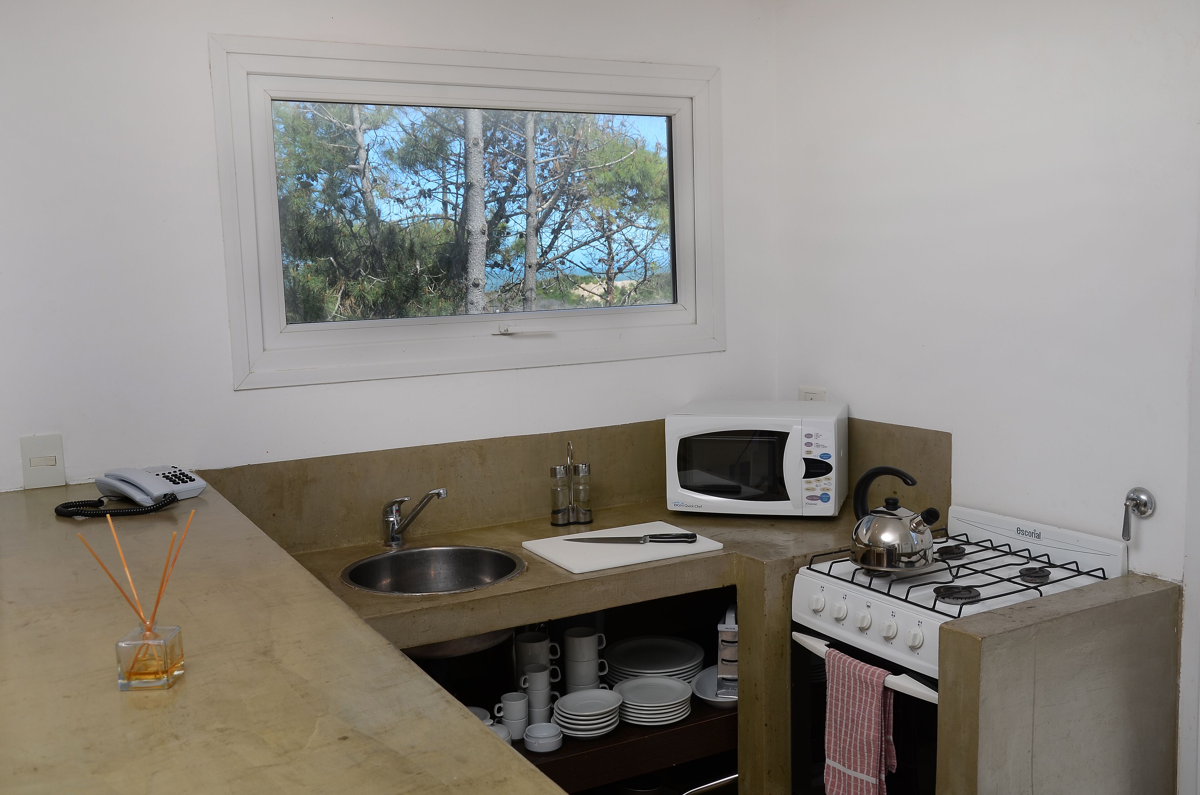 Cozinha compacta com janela, micro-ondas, fogão a gás, pia e armário pequeno.
