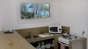 Cozinha compacta com janela, micro-ondas, fogão a gás, pia e armário pequeno.
