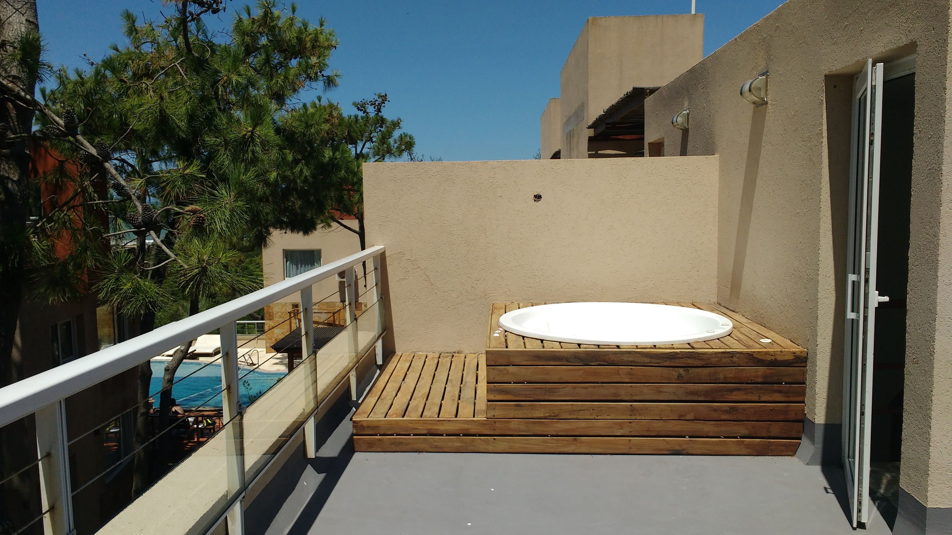 A rooftop terrace with a hot tub, wooden deck, and a glass balustrade.